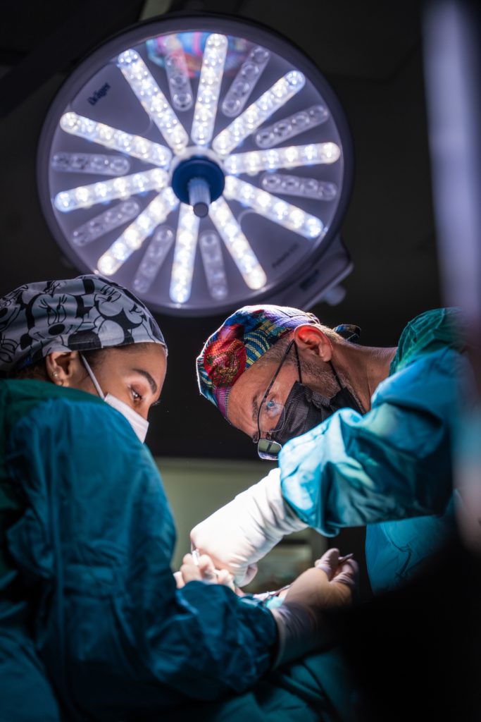 Doctor and nurse in scrubs performing surgery with light above them, healthcare
